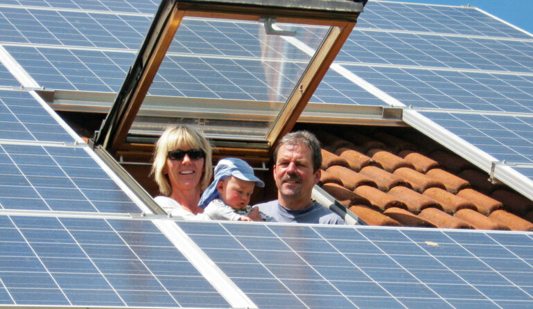 Familie schaut aus dem Dachfenster zwischen Solarpanels.