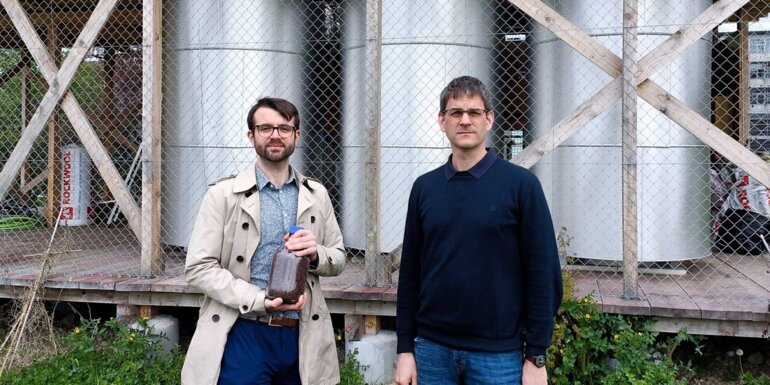 Die ETH-Forschenden Samuel Heiniger (links, mit einem Glas Eisenerz) und Professor Wendelin Stark vor den drei Eisenreaktoren am Campus Hönggerberg der ETH Zürich.  (Bild: ETH Zürich)
